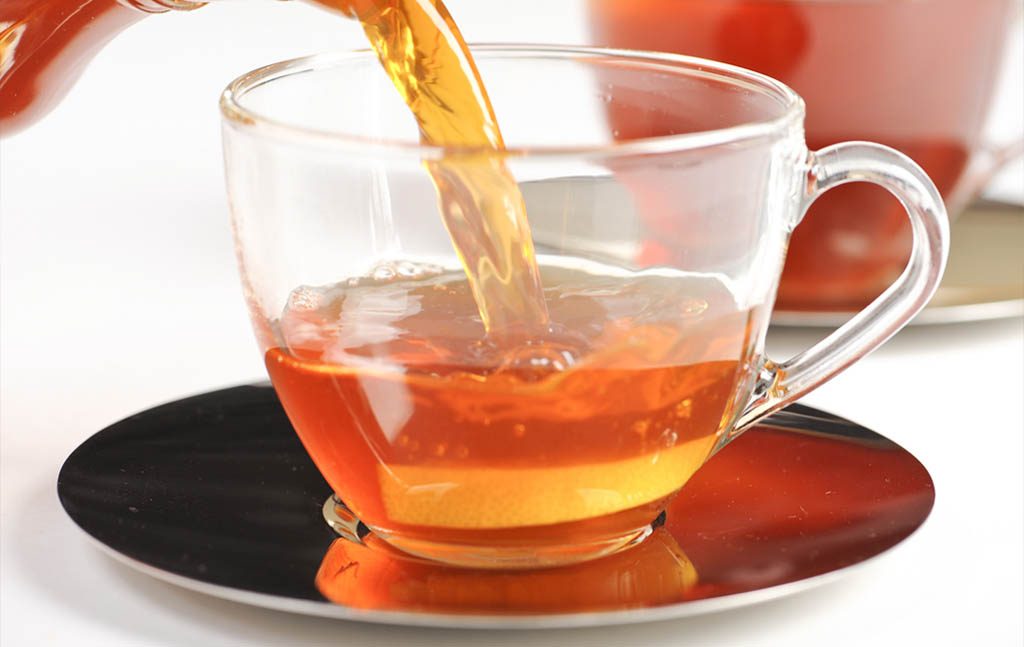 a clear cup of rooibos tea with teapot in the background.
